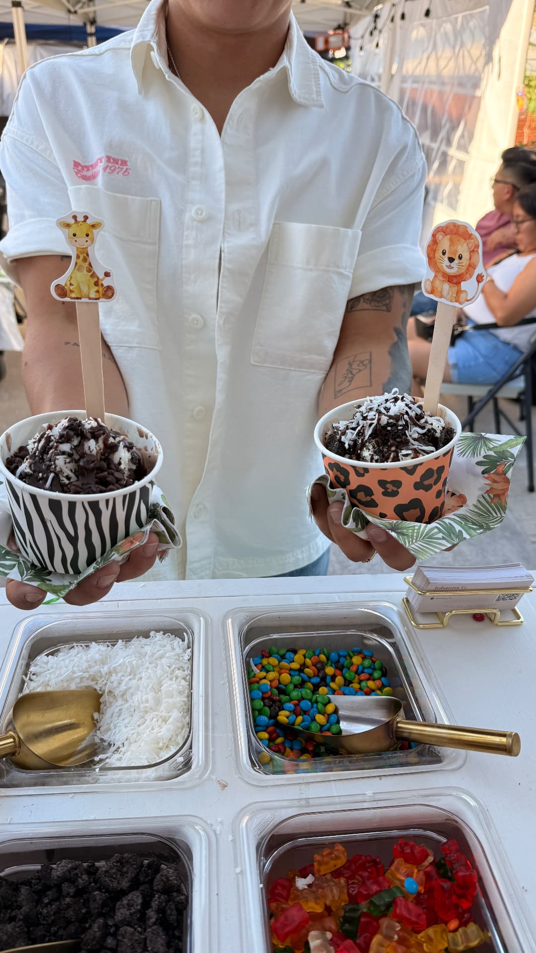 Two decorated ice cream cups held above topping trays