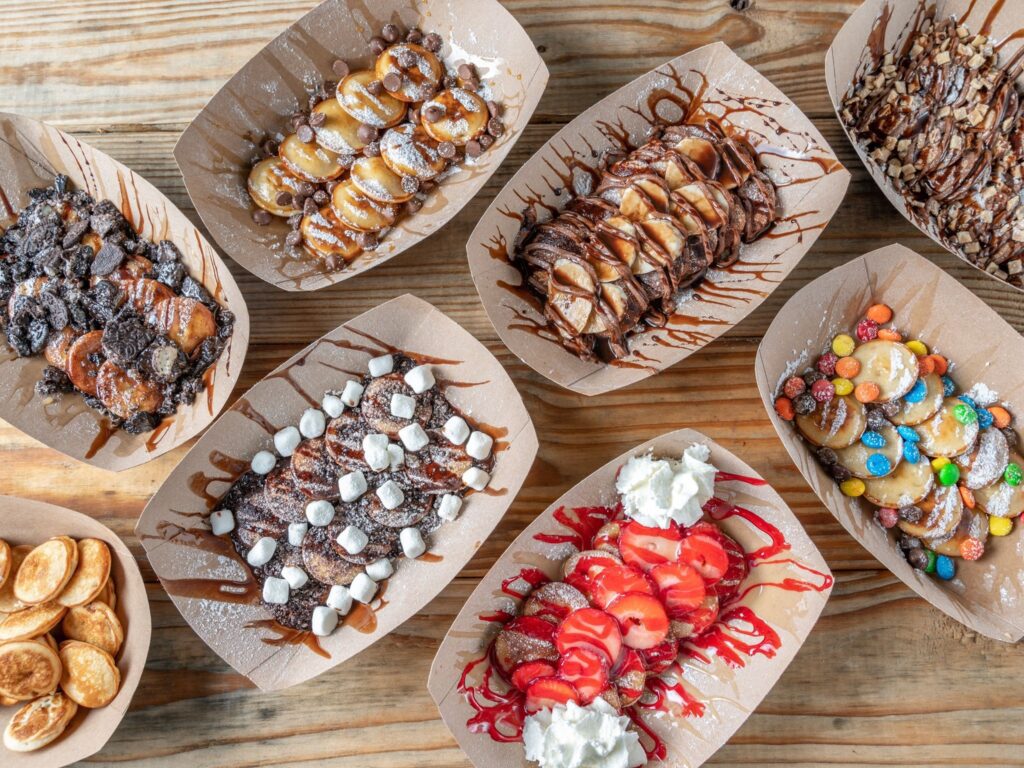 Mini pancakes in checkered boats surrounded by topping trays